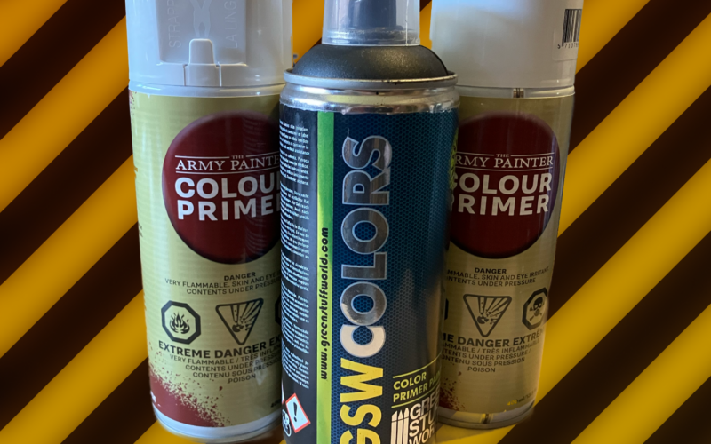 Two cans of Army Painter and a can of Green Stuff World primer on a hazard stripe background.